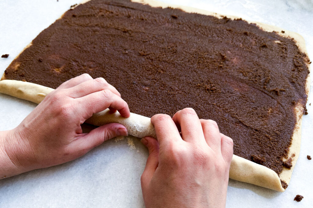 A person rolling the dough for cinnamon rolls into a log.