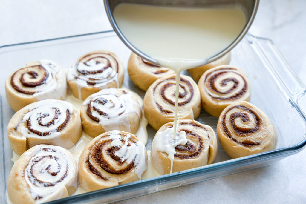 Unbaked cinnamon rolls in a pan with cream being poured on top.